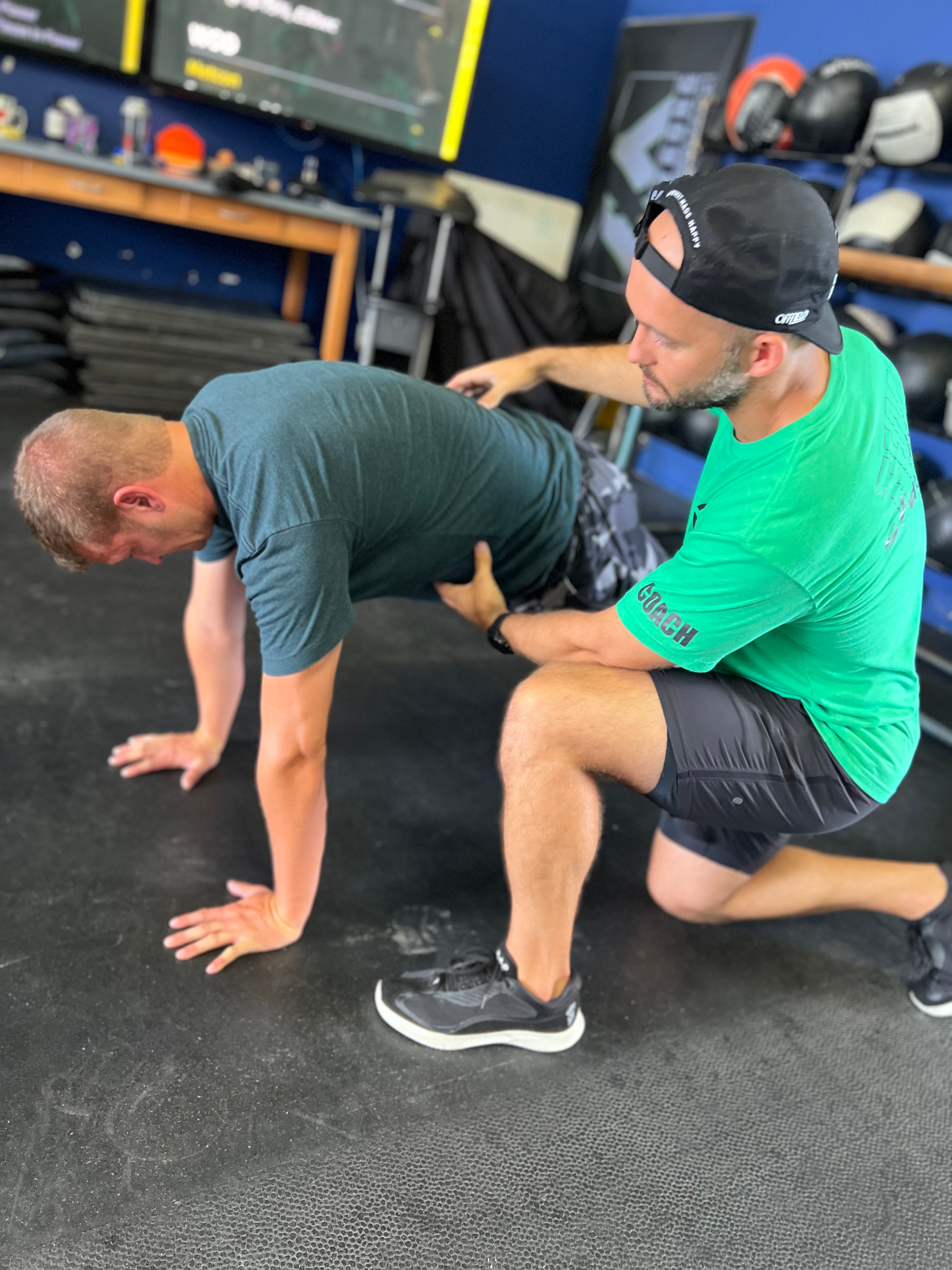 A man in a green shirt is helping another man do push ups