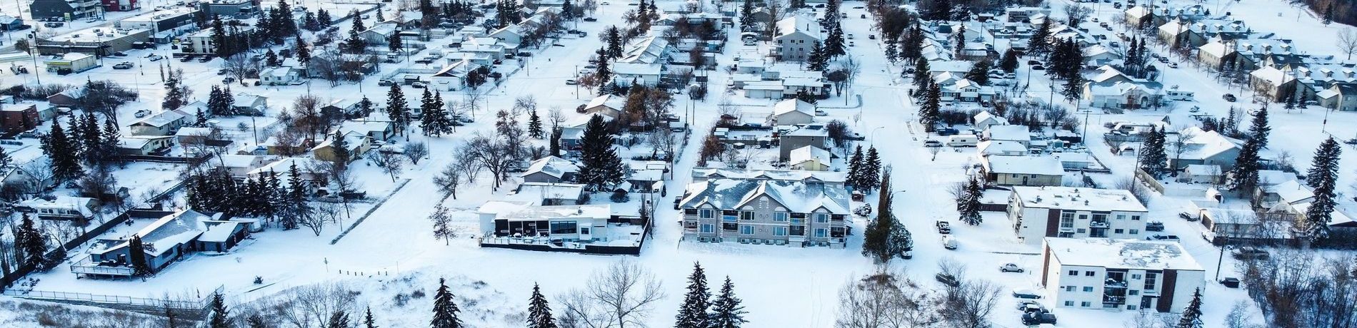 An aerial view of a snowy town with houses and trees covered in snow.