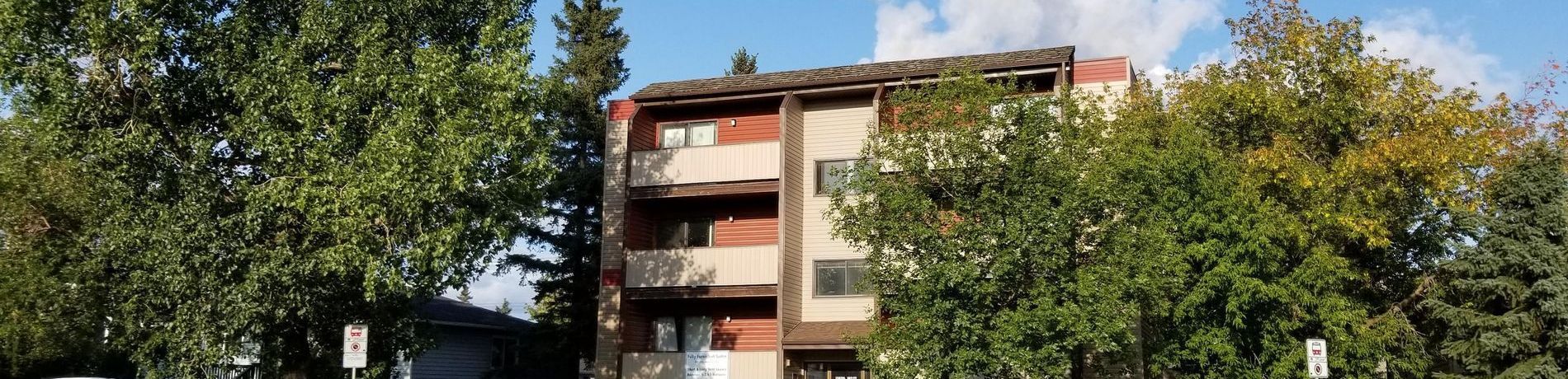 A large apartment building surrounded by trees on a sunny day.