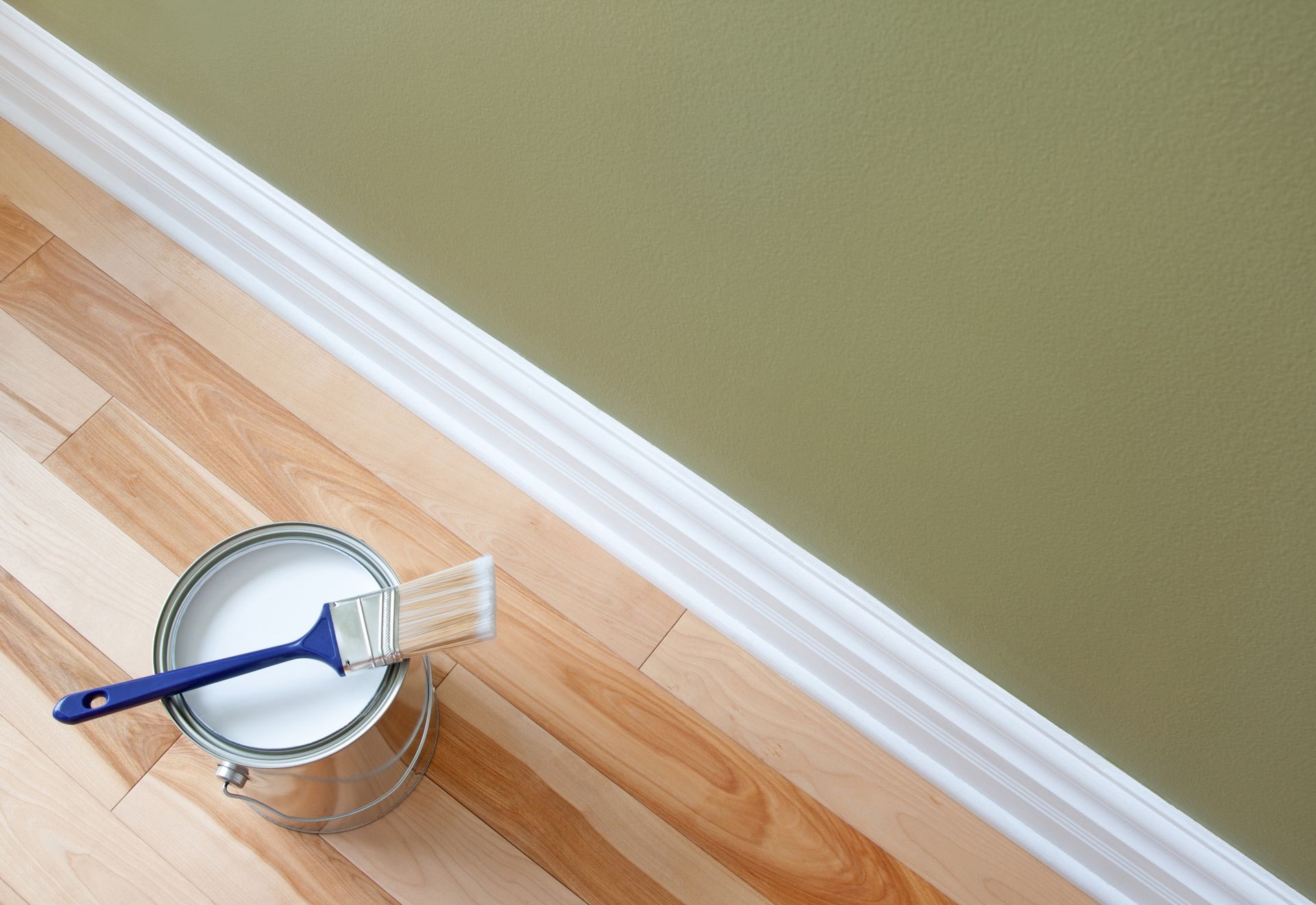 A can of paint and a brush on a wooden floor