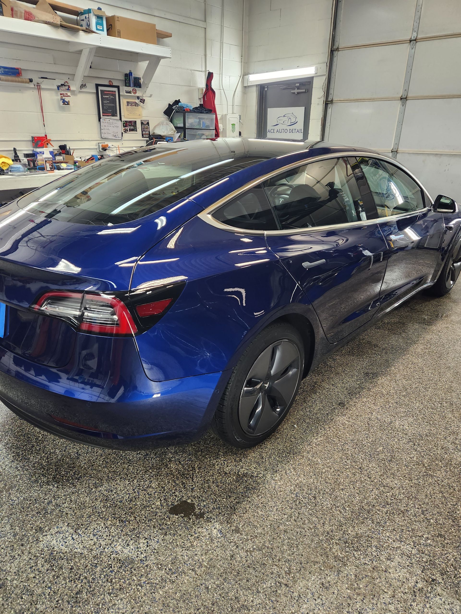A blue tesla model 3 is parked in a garage.