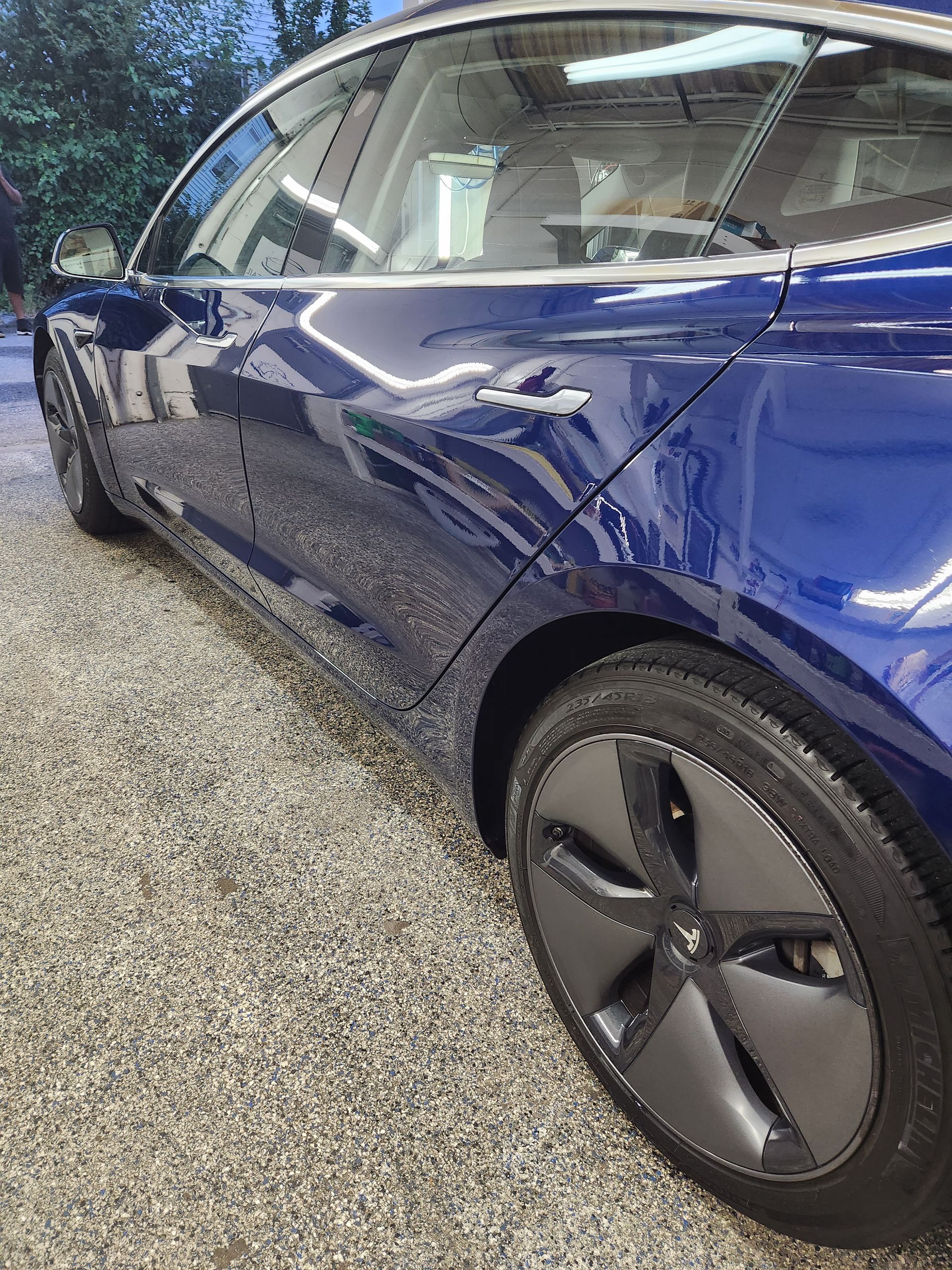 A blue tesla model 3 is parked in a garage.