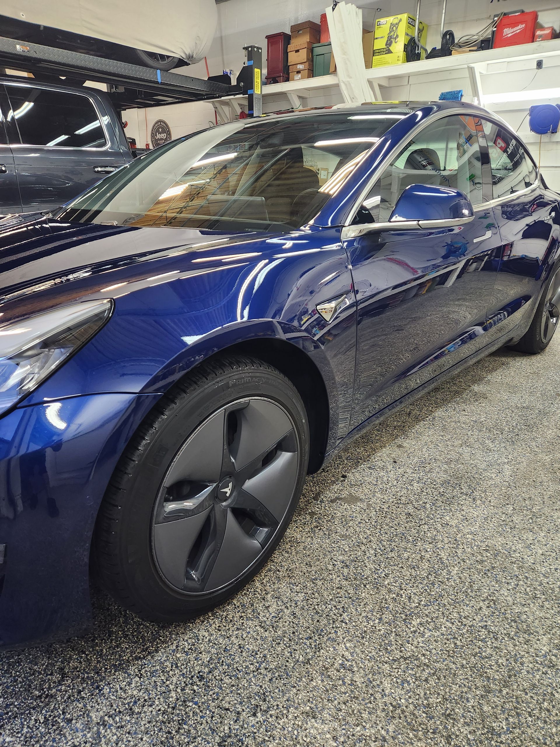 A blue tesla model 3 is parked in a garage.