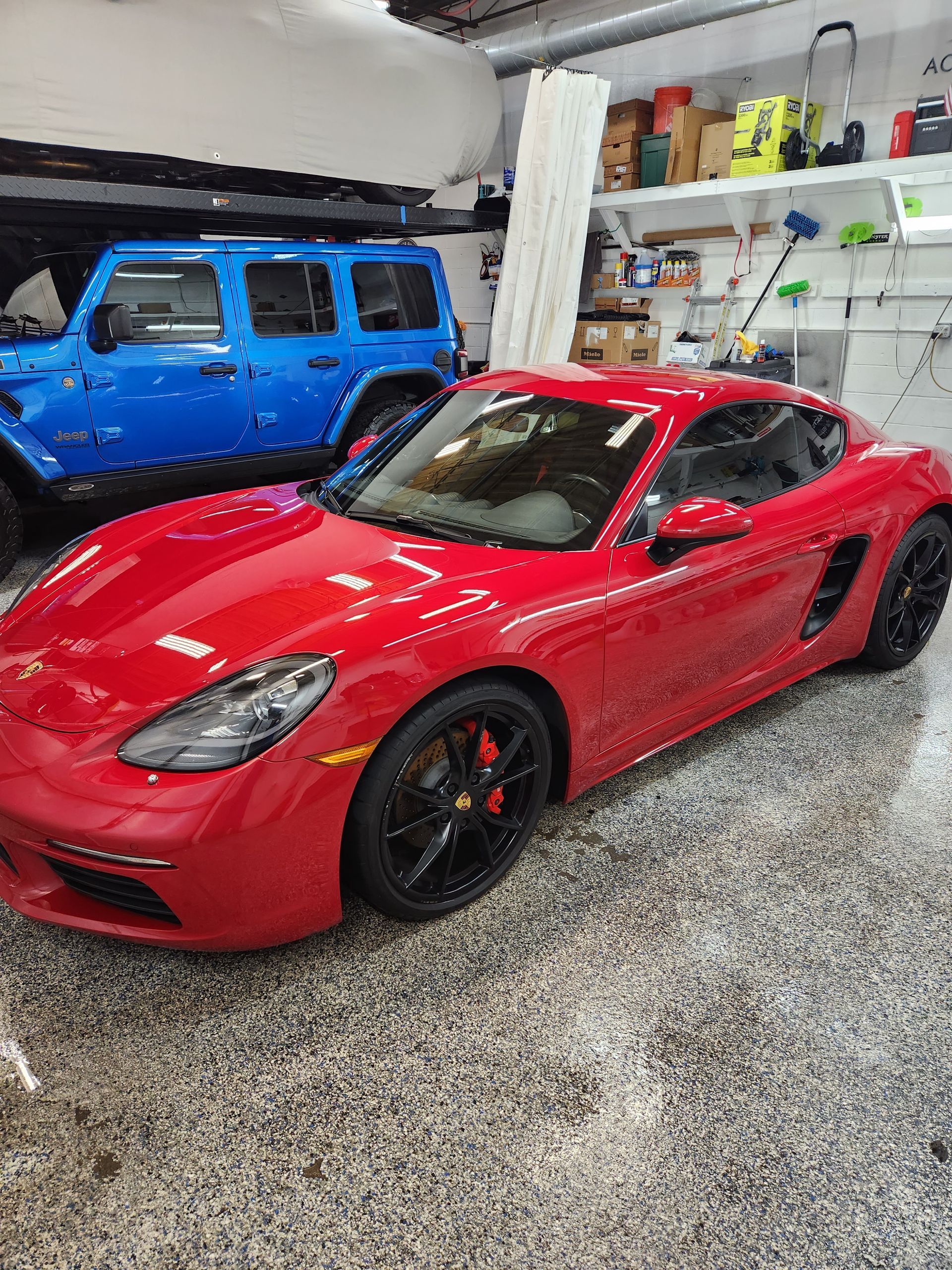 A red porsche boxster is parked in a garage next to a blue jeep.