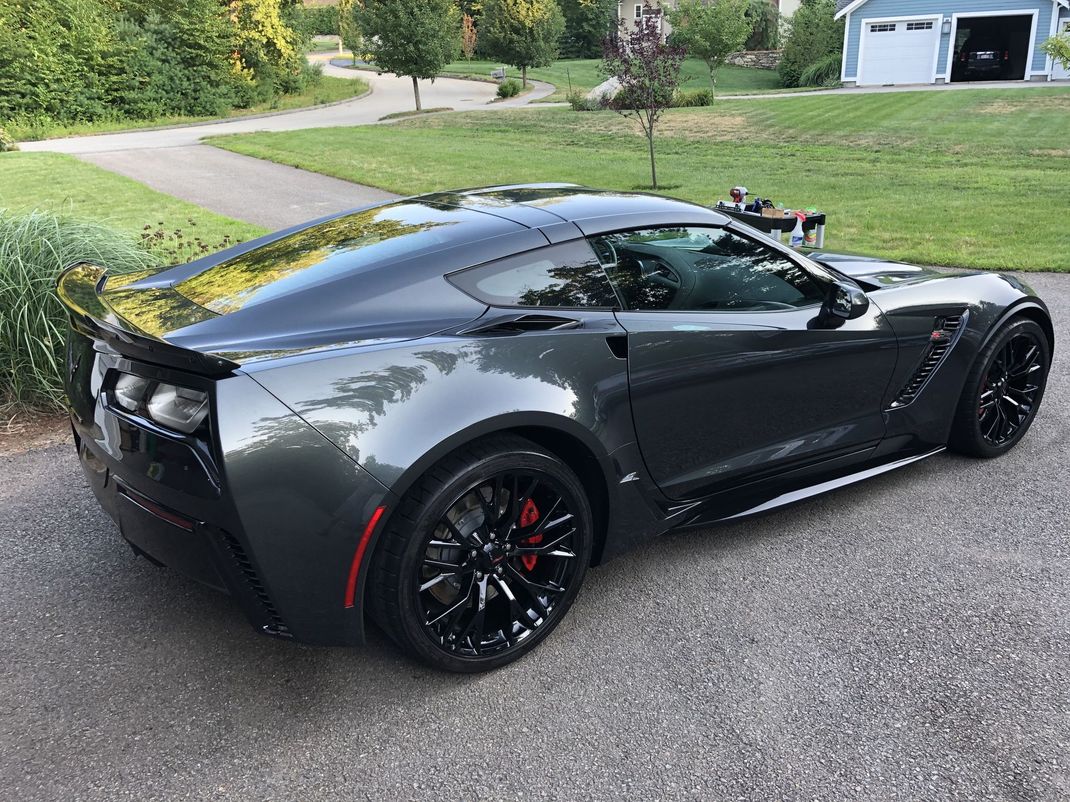 A gray sports car is parked in a driveway next to a garage.