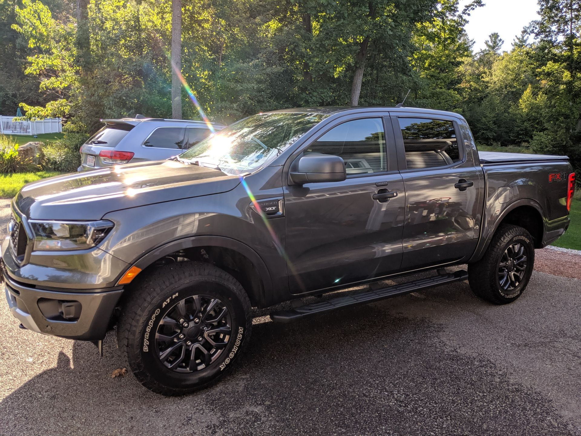 A gray Ford Ranger pickup truck parked on a gravel surface outdoors with trees in the background.