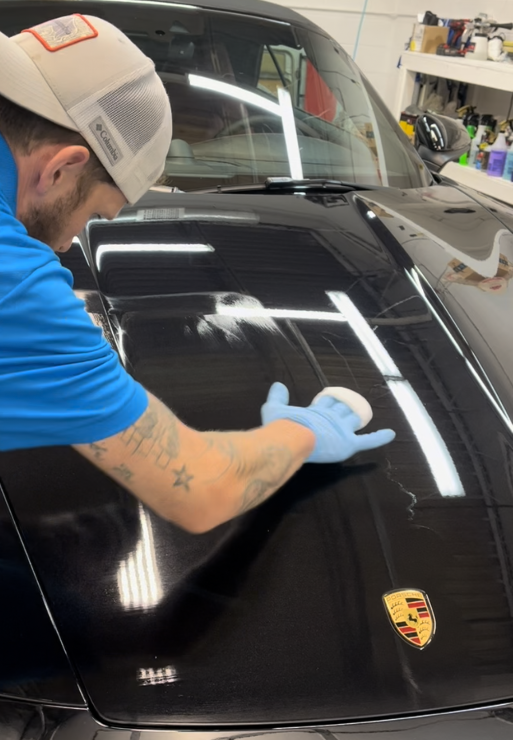 A man is polishing the hood of a black car.