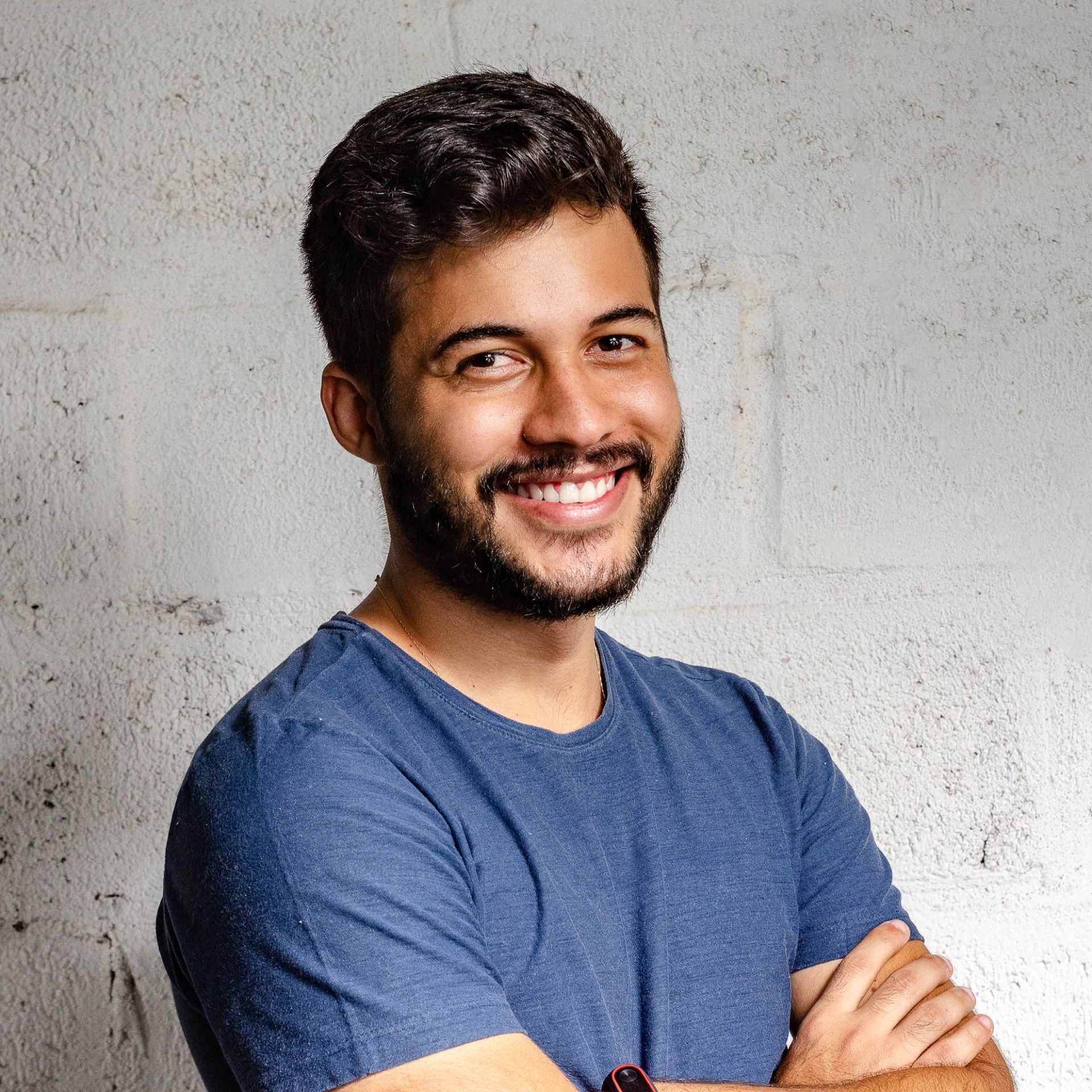 A man with a beard is wearing a blue shirt and smiling with his arms crossed.