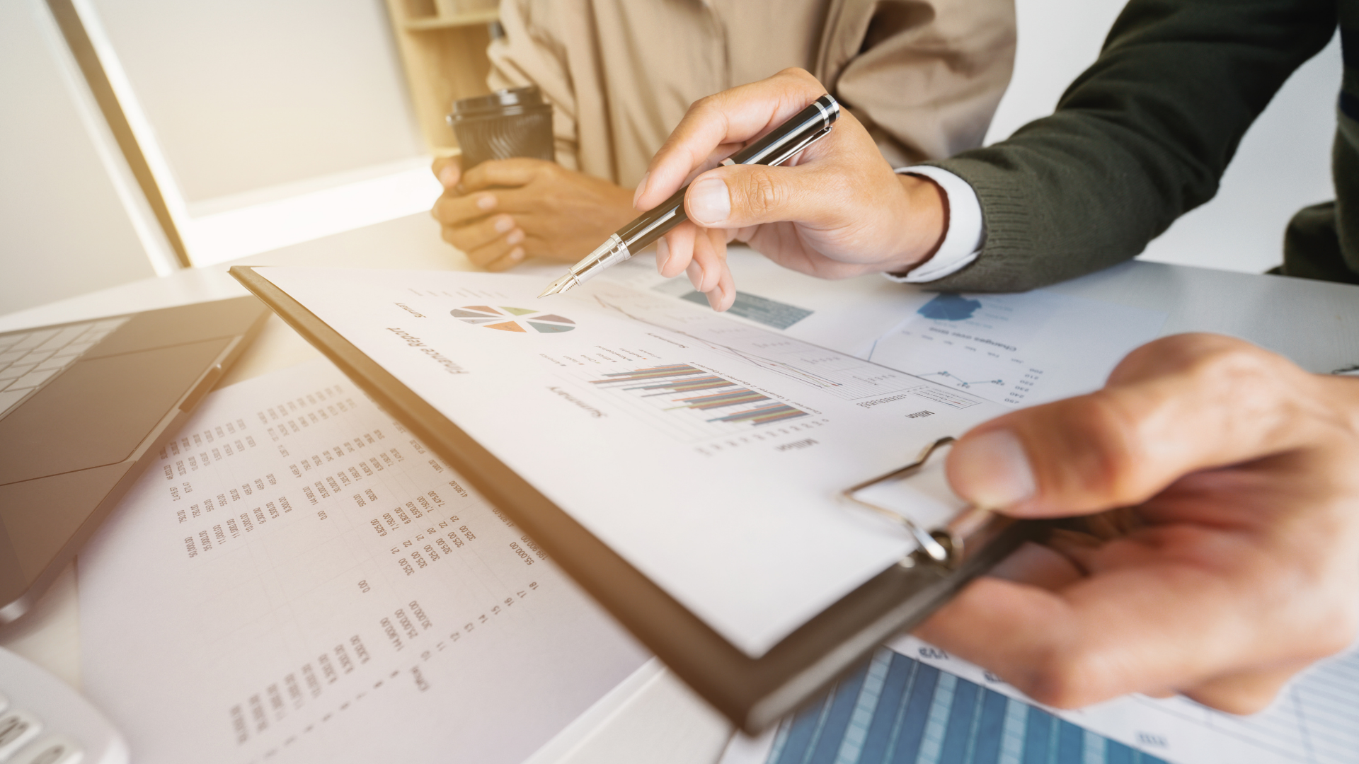 Two people reviewing financial charts with a pen, indoors.