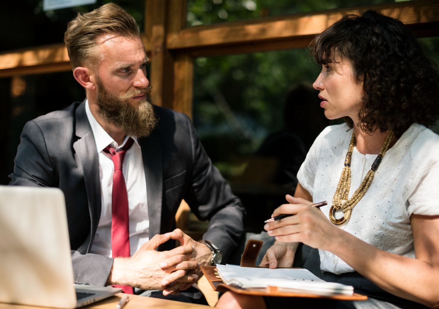Two people in business attire talking at a table in a sunlit café