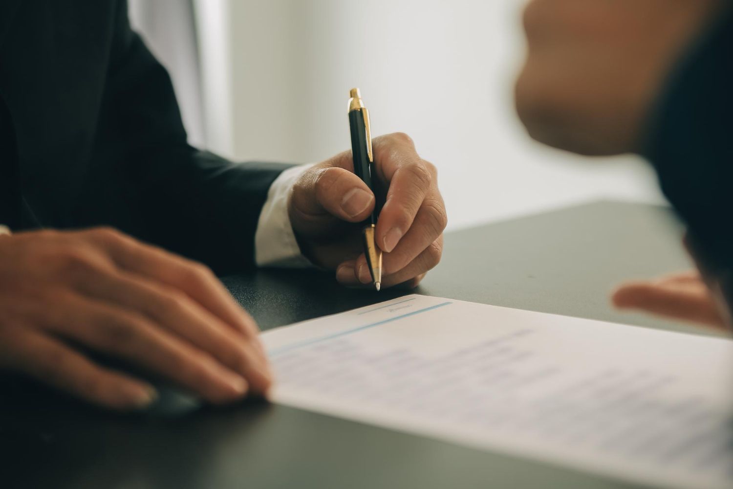 Hands signing a document at a table with a pen.