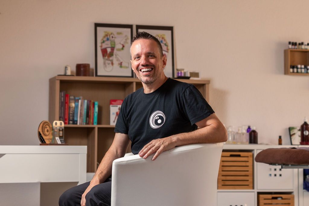 Un homme est assis sur une chaise dans une pièce et sourit.