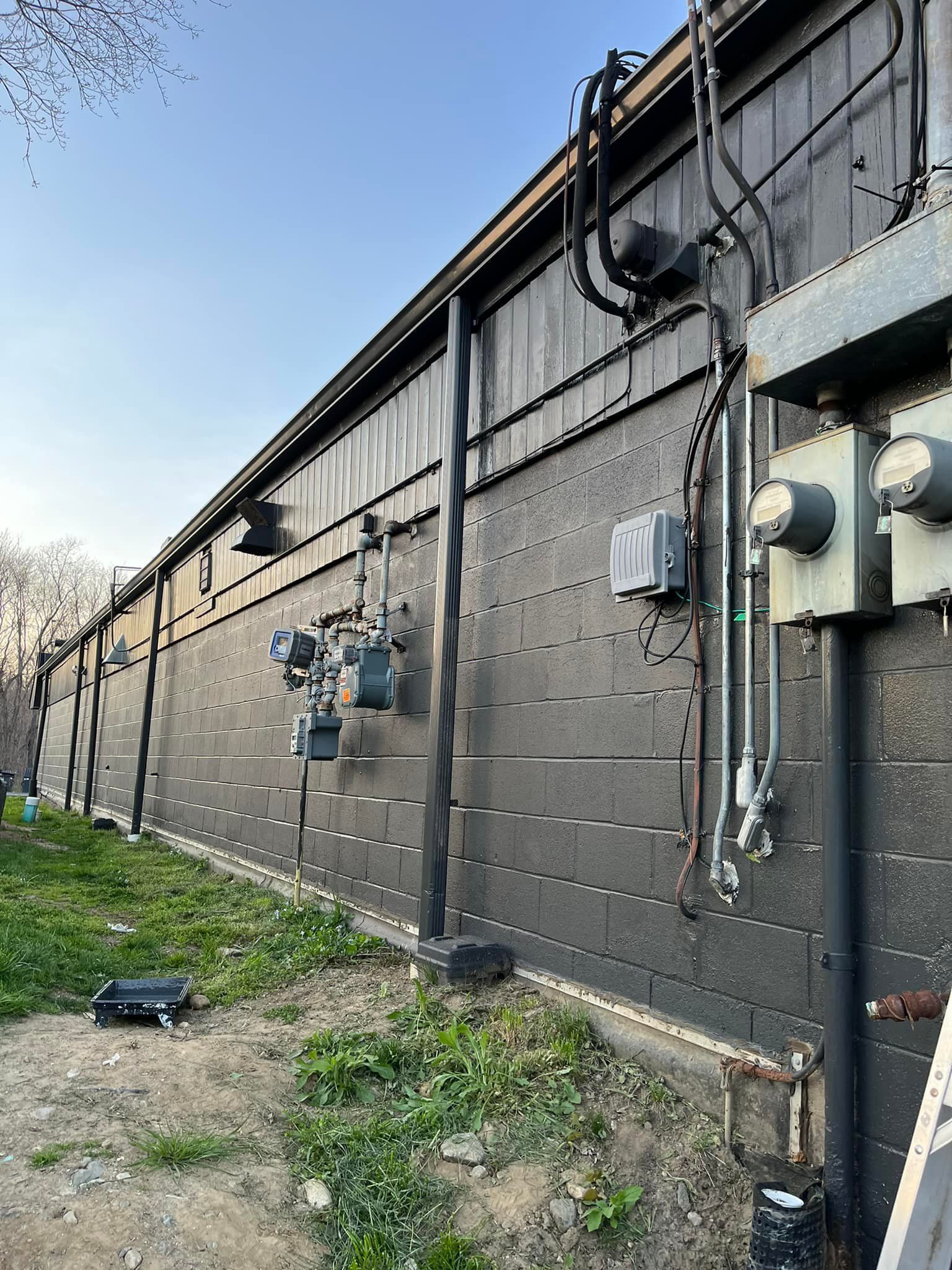Exterior of a black painted building with electrical boxes, pipes, and meters on the side.