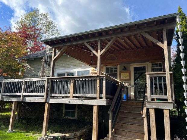 Wooden house with deck and covered porch, green roof, autumn trees.