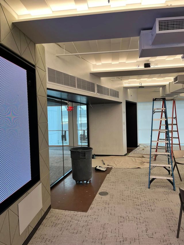 Interior view of an office space under construction with a large digital screen, a grey trash bin, and two ladders.