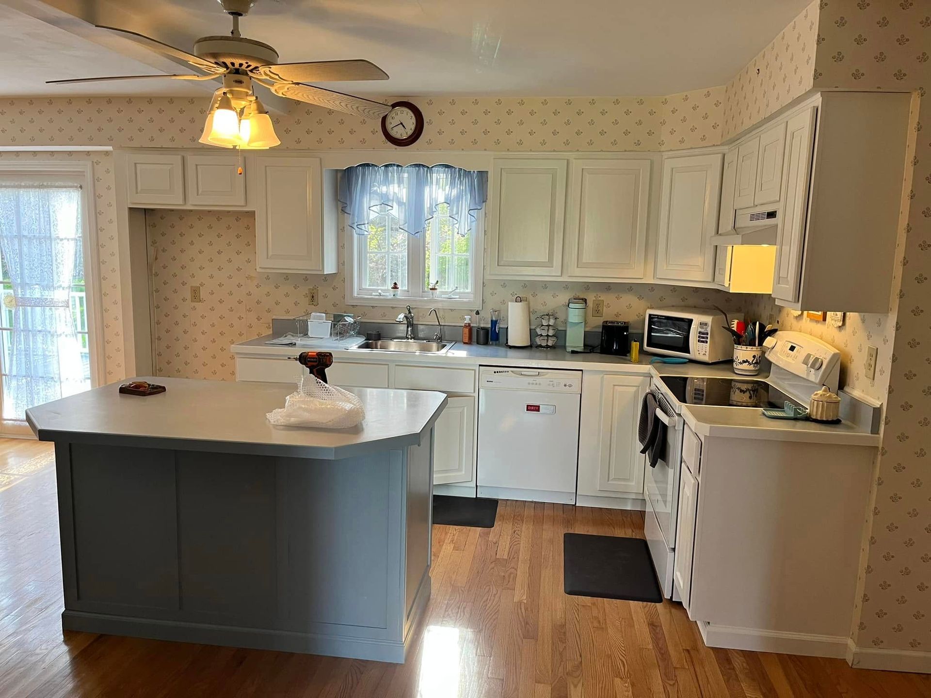Kitchen with white cabinets, island, and wooden floor. A sliding door and window are present.