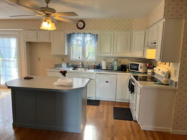 Kitchen with white cabinets, island, and wooden floor. A sliding door and window are present.