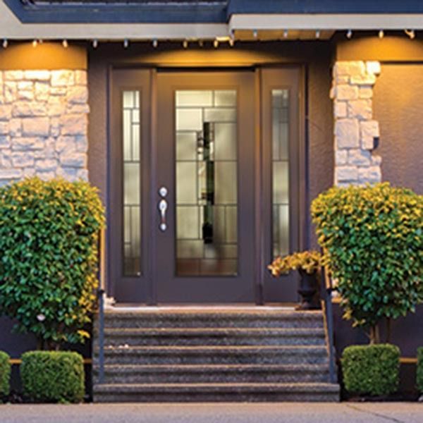 Front entrance with dark wood double doors, stone facade, steps, and trimmed bushes at dusk