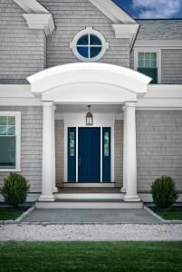 Front entrance of a gray house with blue double doors, white columns, and a circular window above the porch.