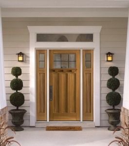 Wooden double front doors with white trim, flanked by topiary planters and wall lanterns on a porch