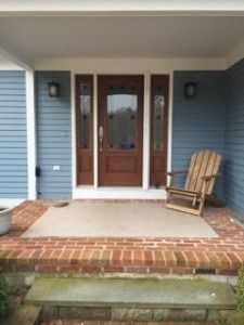 Front porch with blue siding, brick steps, glass double doors, and a wooden chair on the right.