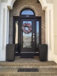 Front door with a wreath on a brick house, framed by dark pillars and steps.