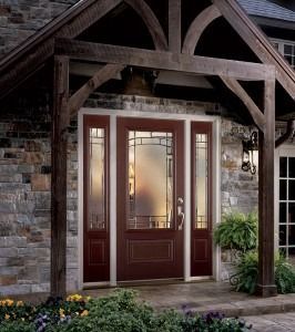 Front door with glass panels beneath a rustic wooden porch overhang, flanked by brick and potted greenery