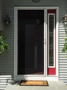 Front door with a glass sidelight and red trim, open to a dark interior, with a doormat on the porch.