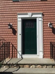 Front entrance with dark green door, white trim, and brick facade between two wall lanterns.