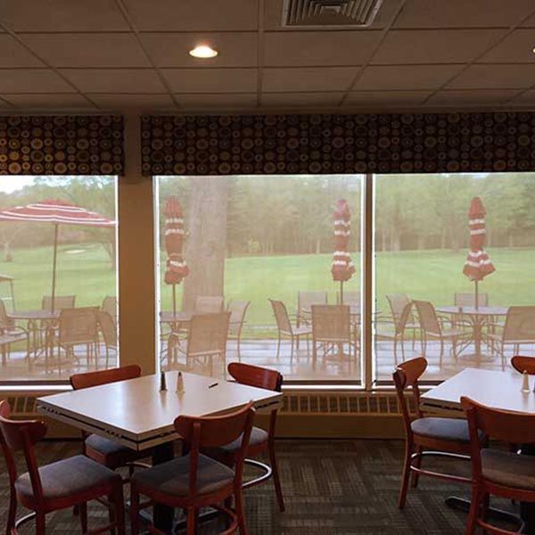 Empty dining area with tables and chairs by large windows overlooking a rainy green patio