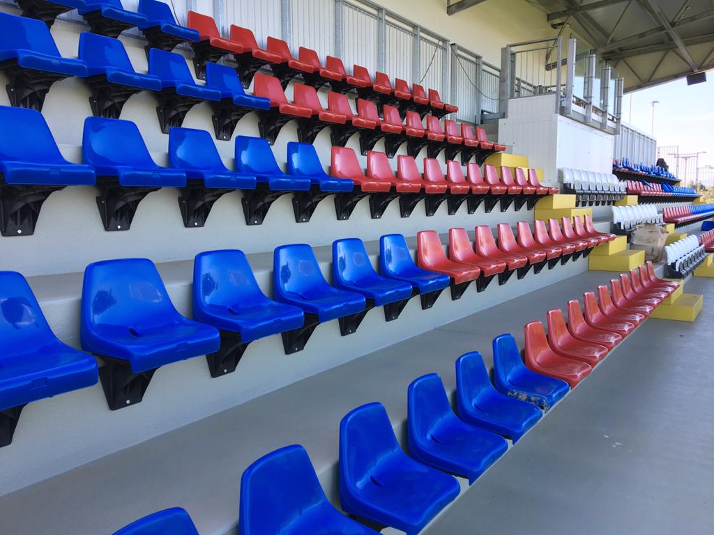 Una fila di sedili di plastica blu e rossi in uno stadio.