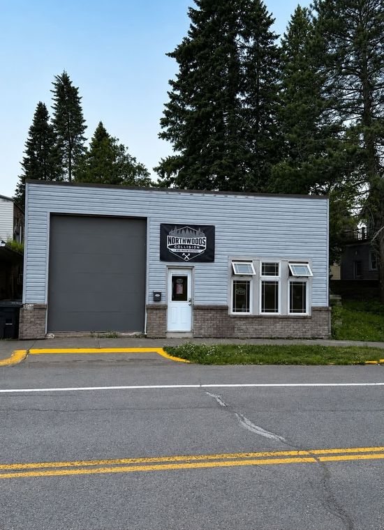 Small gray storefront with a garage door, windows, and a sign along a roadside.