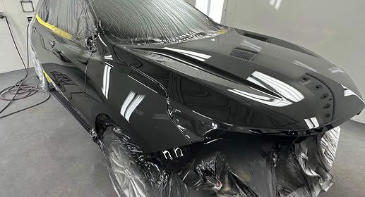 Black car hood and front end in a body shop, partially covered with masking plastic during repair or painting