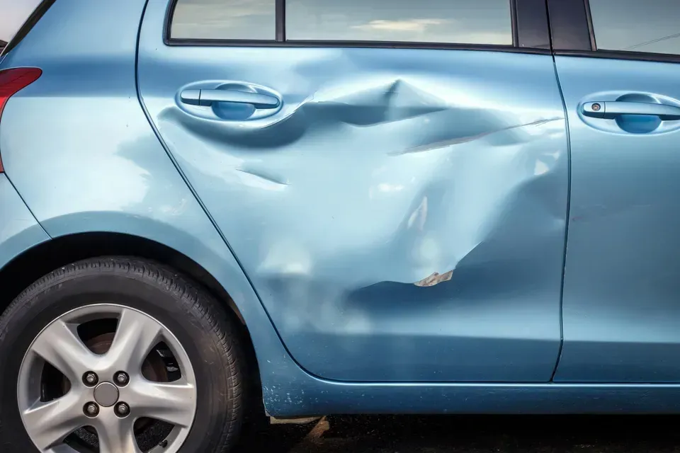 Blue car with a large dent in the rear door and side panel