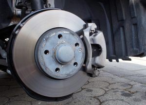 Close-up of a car’s front brake rotor and caliper on a paved surface.