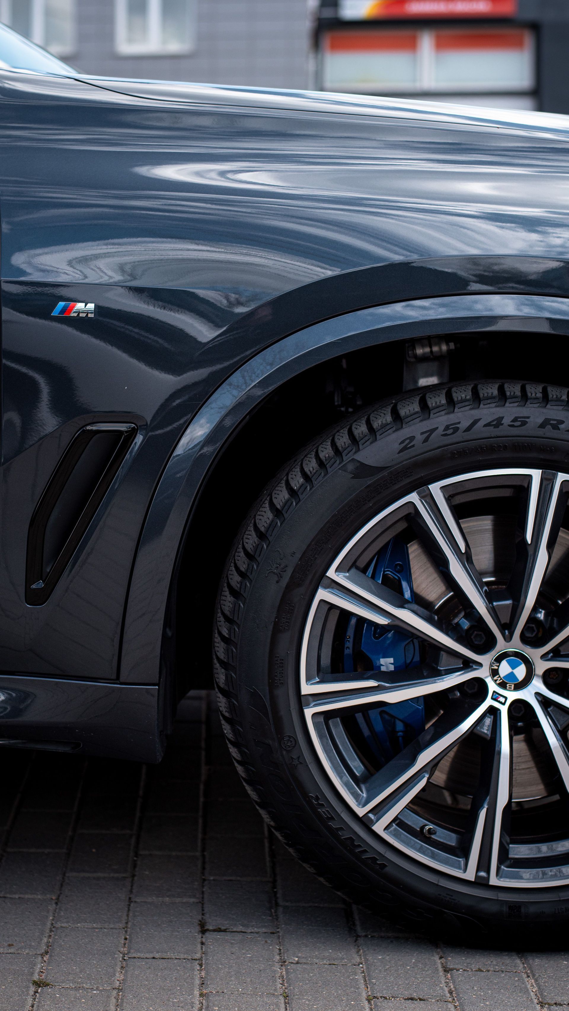 Close-up of a dark gray BMW car’s front wheel and fender on a paved street.