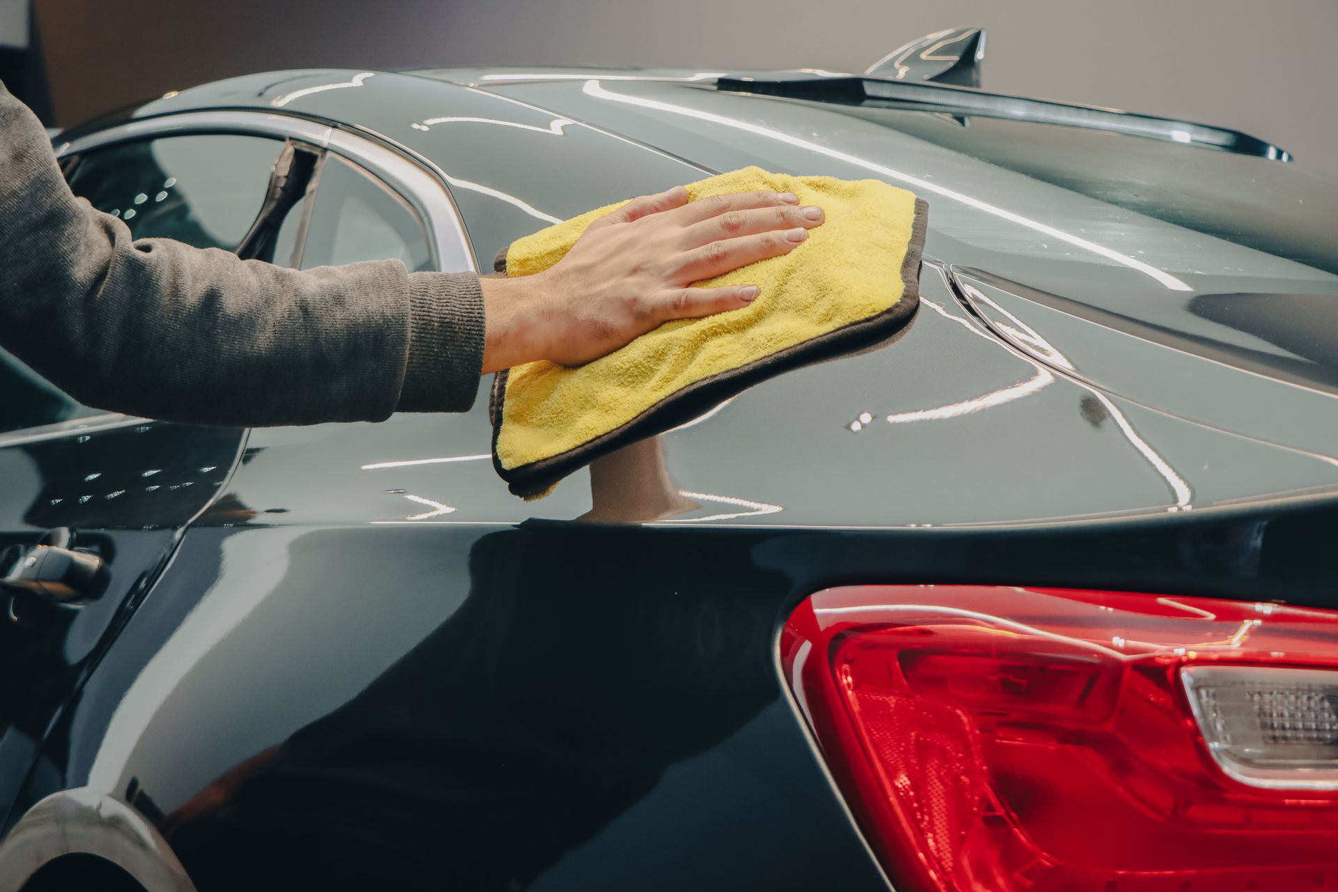 Hand wiping a black car’s roof with a yellow cloth near the rear taillight
