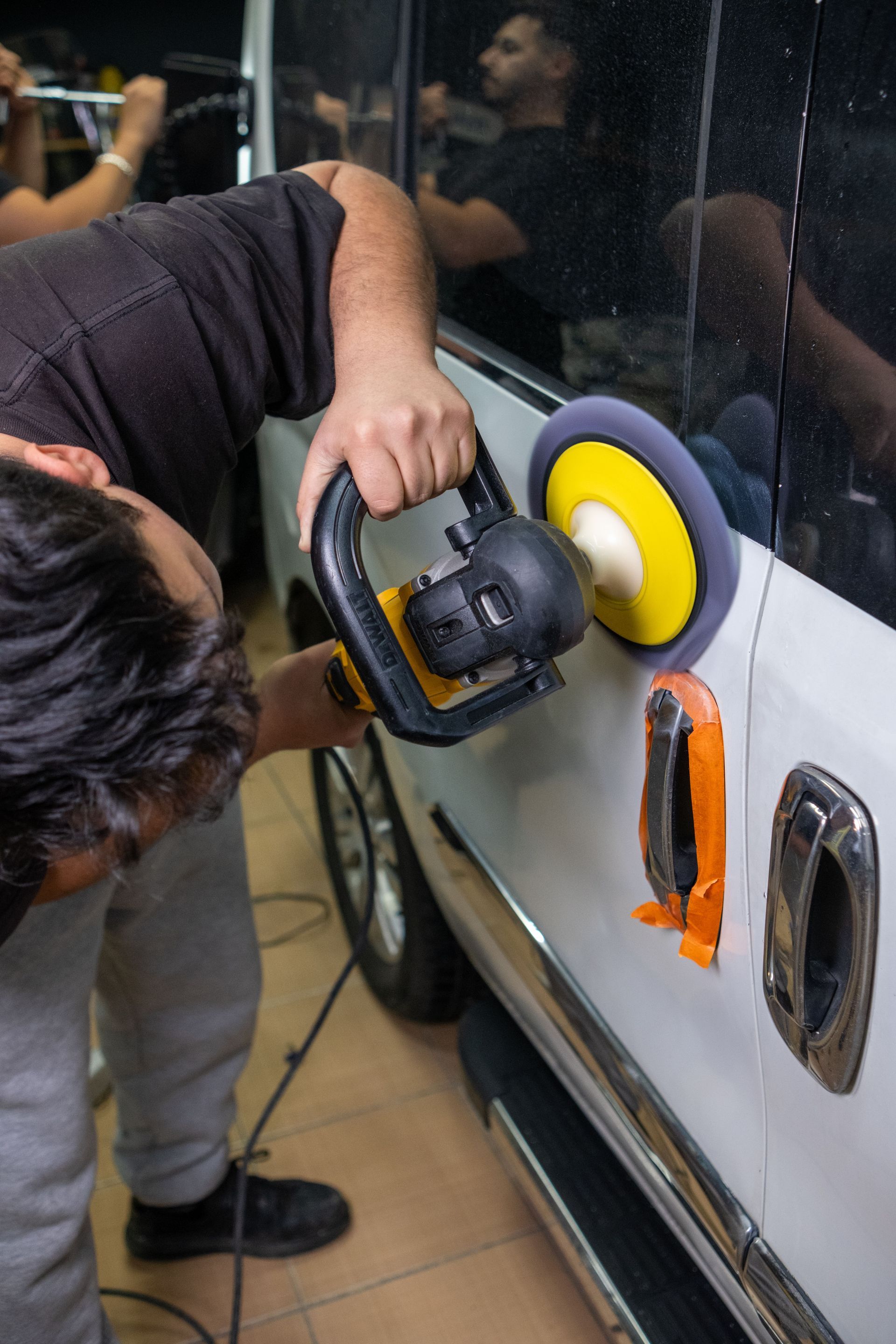 Person using a buffer to polish a car door beside a window at night