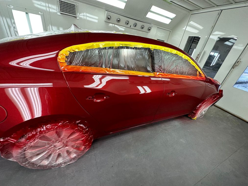 Red luxury car with glossy maroon paint and gold-trimmed windows in a workshop