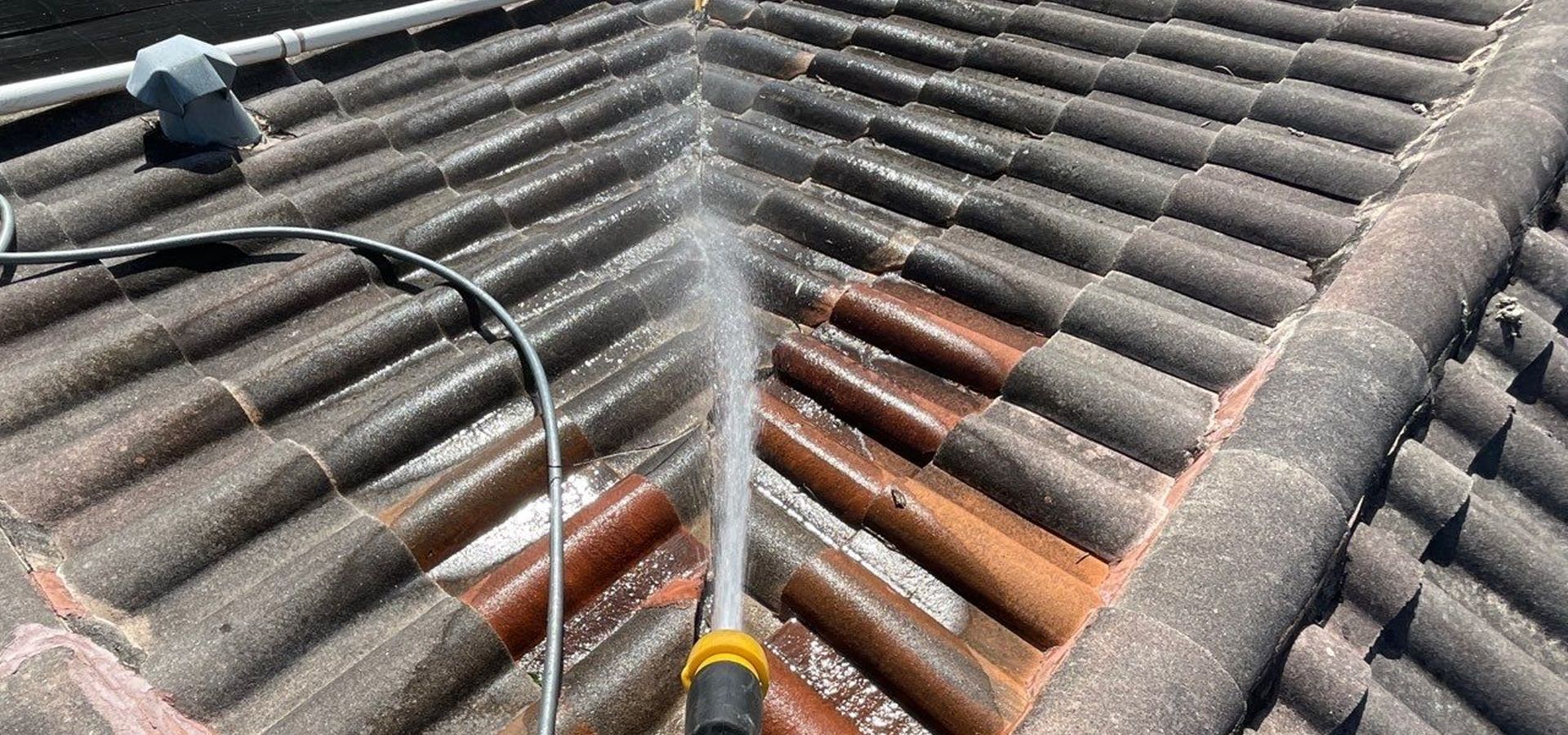 A person hosing down tile roof in Pompano Beach FL as part of roof maintenance