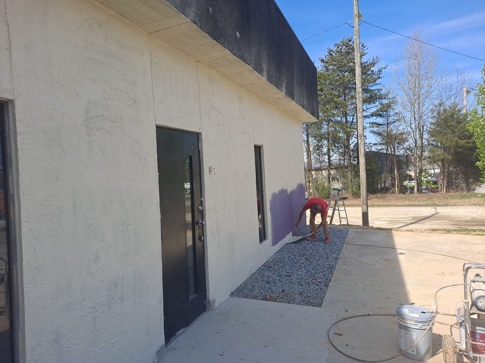 A man in a red shirt is painting the side of a building.