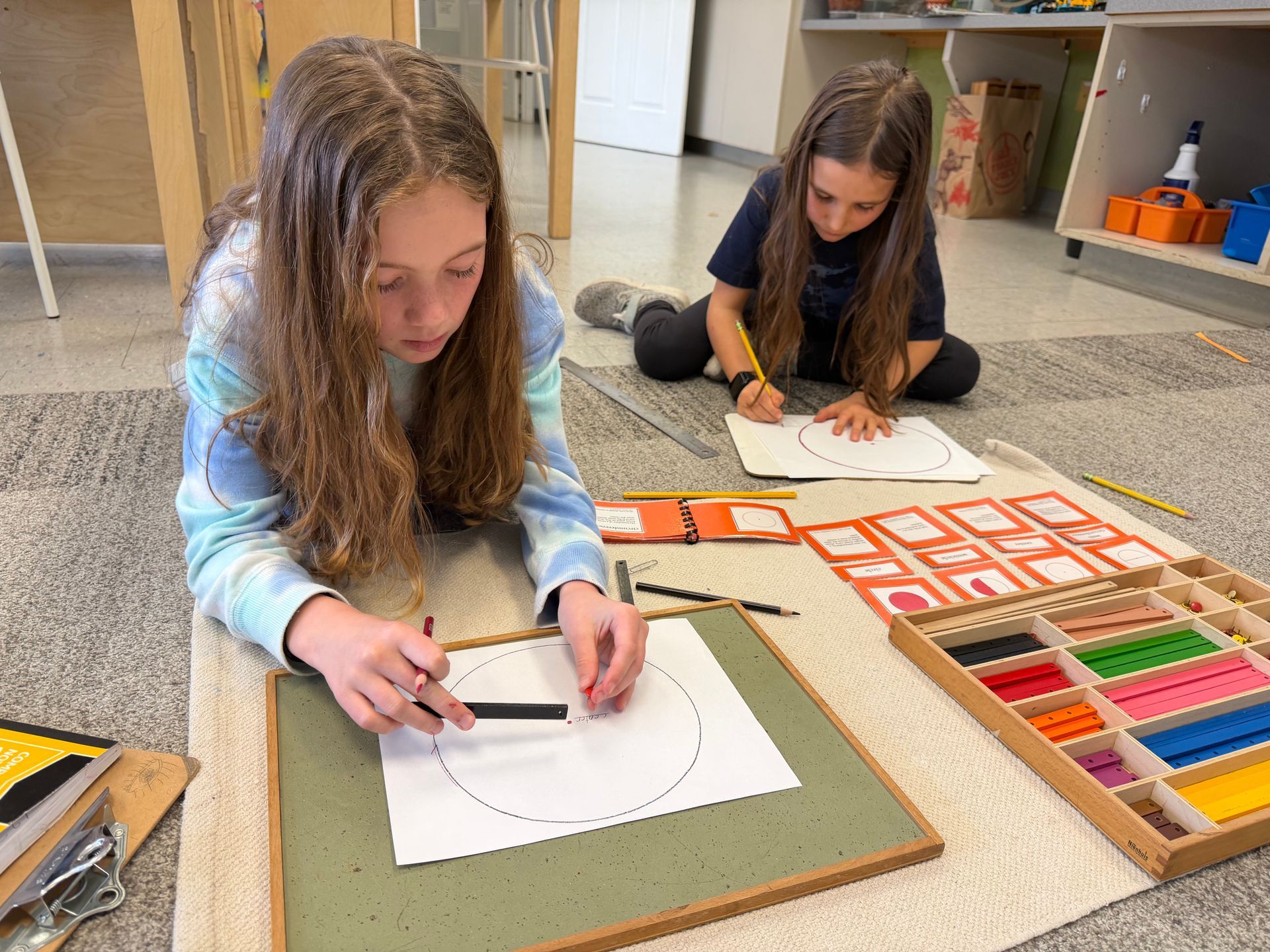 Two children working on large paper in a classroom floor workspace