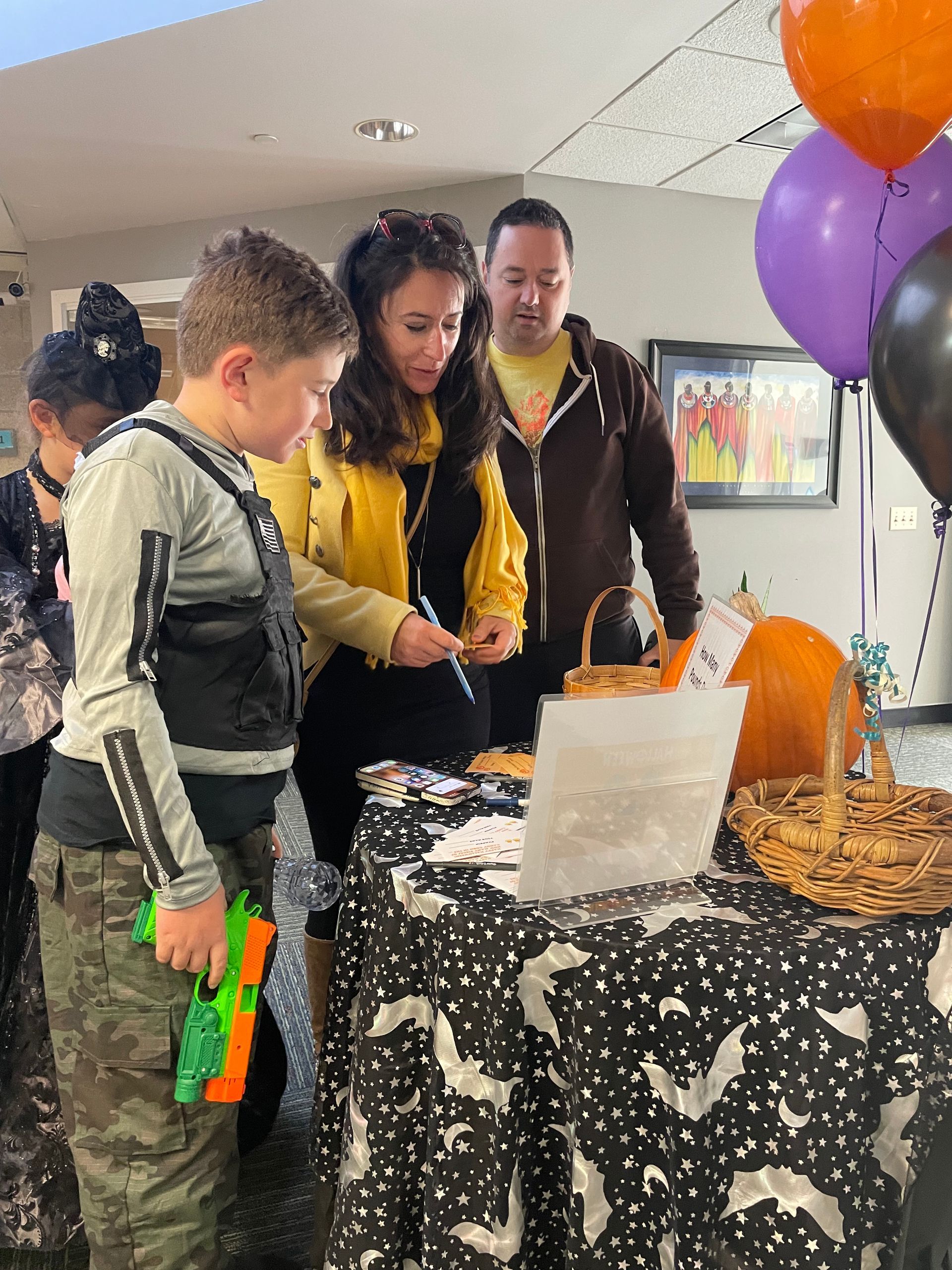 Adults and children gather around a Halloween-themed table, wearing Halloween costumes