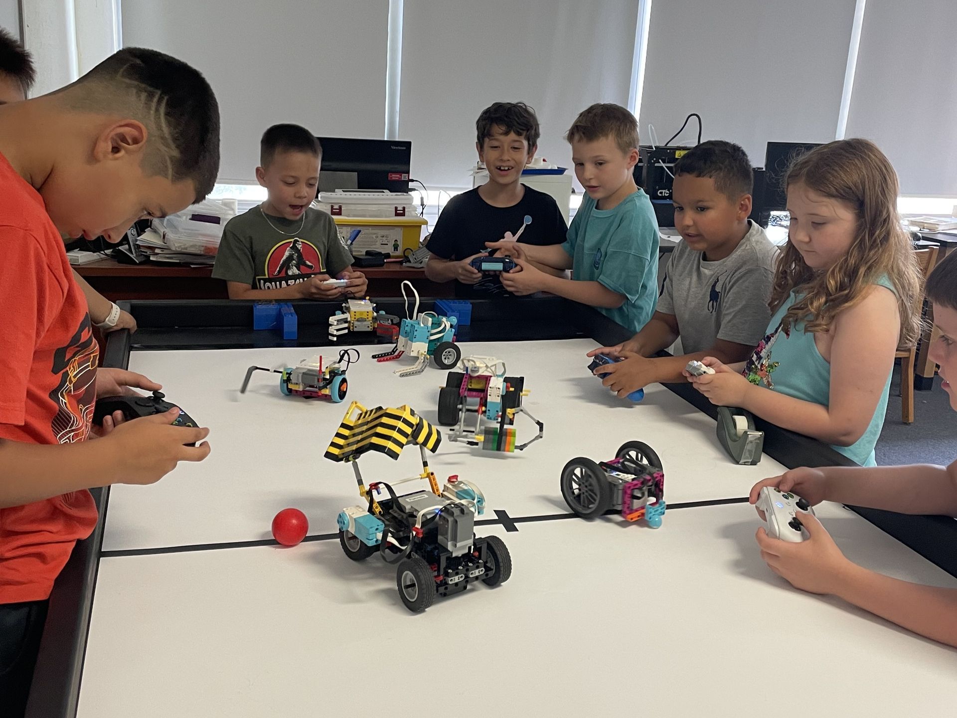 Children using LEGO robots at a classroom table, focused on their builds and controllers.