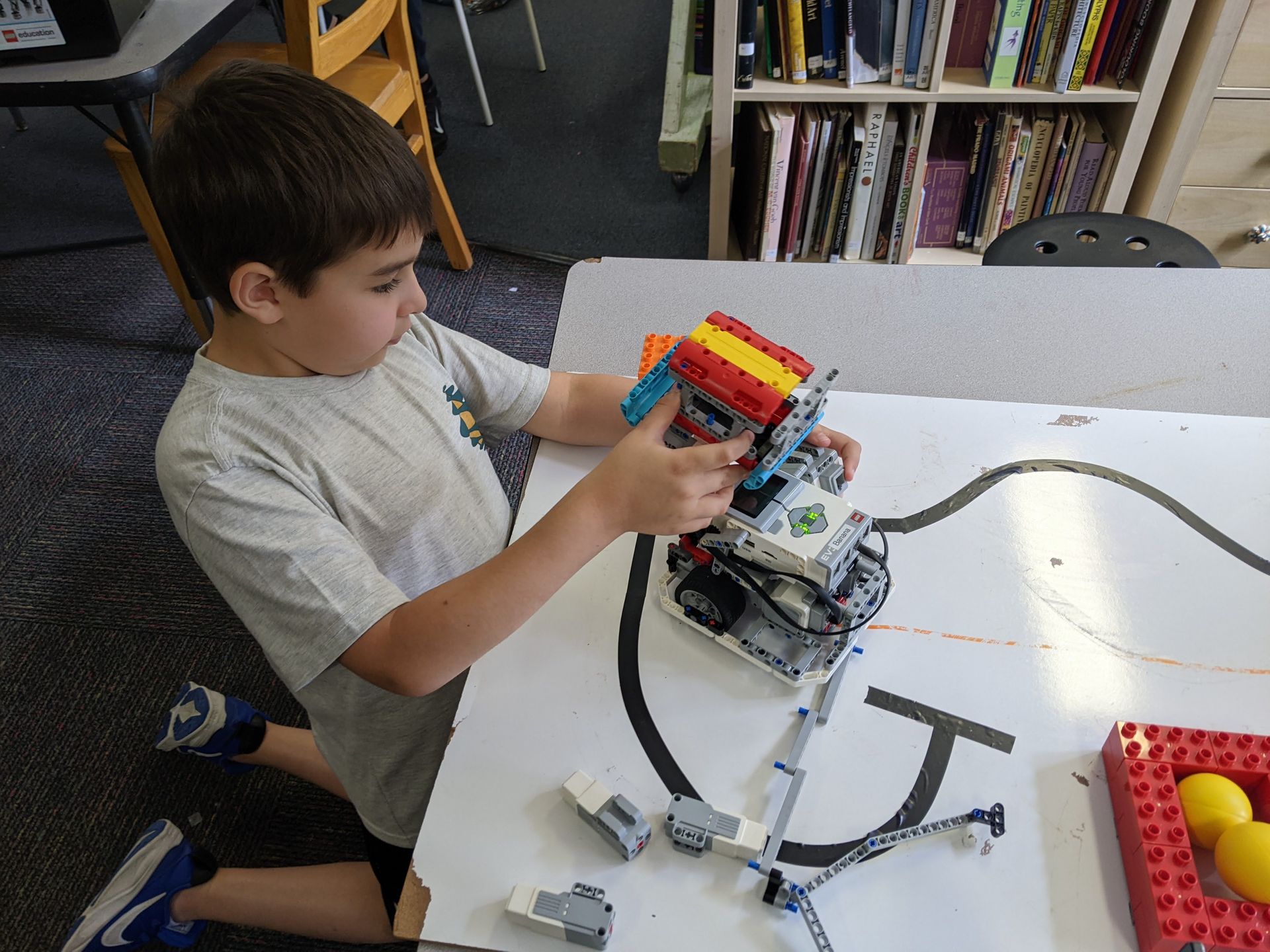 Child assembling a colorful LEGO robot at a white table in a classroom setting