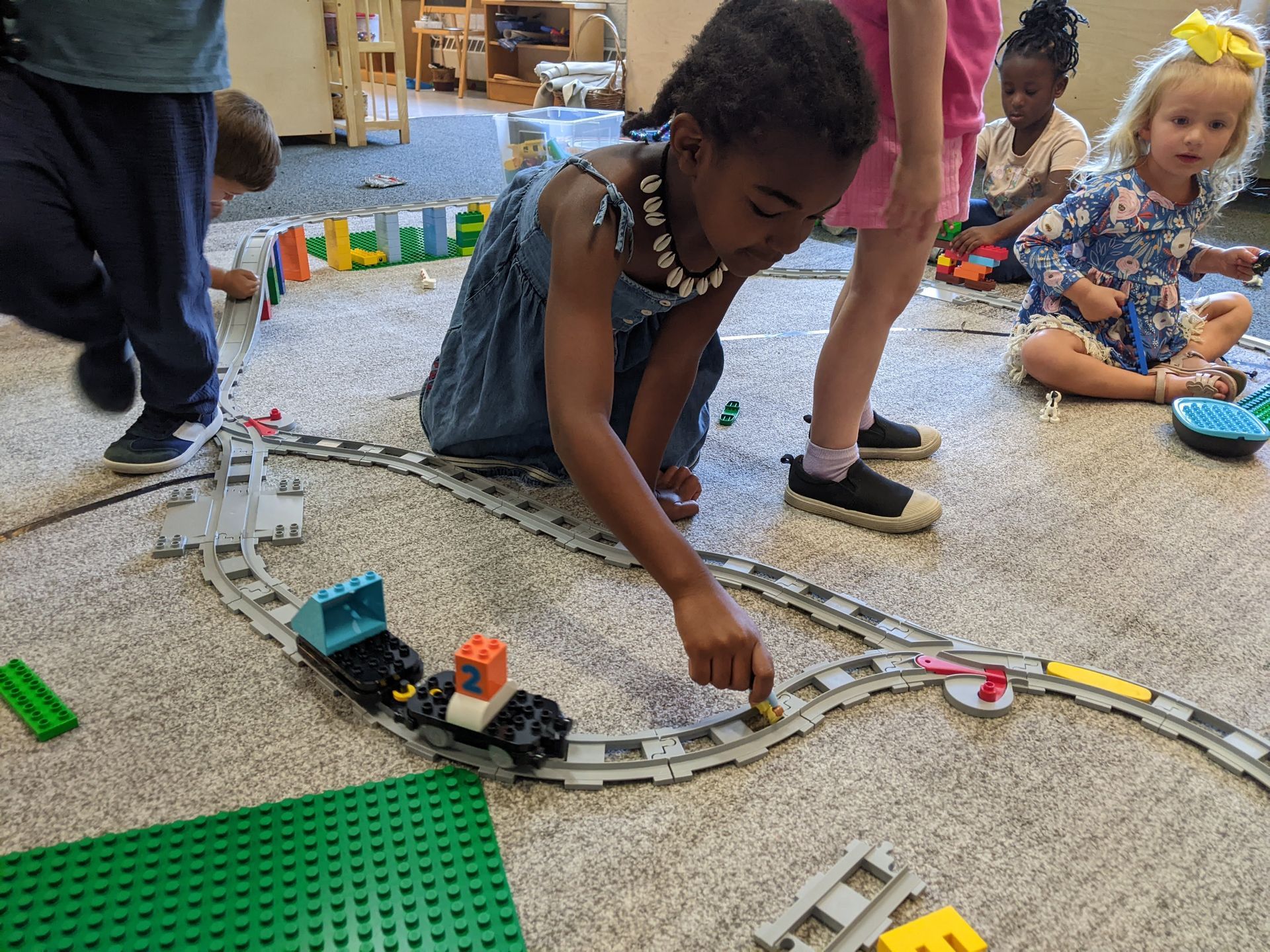 Children playing with a toy train set on a carpeted floor indoors