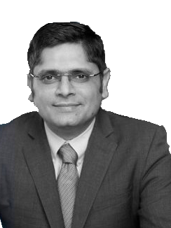 Studio headshot of a man in a suit and tie, wearing glasses, against a plain white background