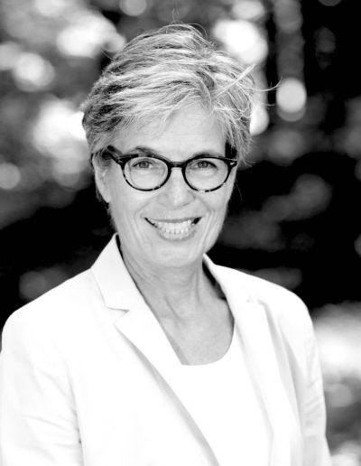 Black-and-white portrait of a smiling person wearing glasses and a light blazer outdoors