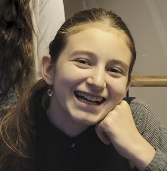 Smiling person resting chin on hand at a table indoors