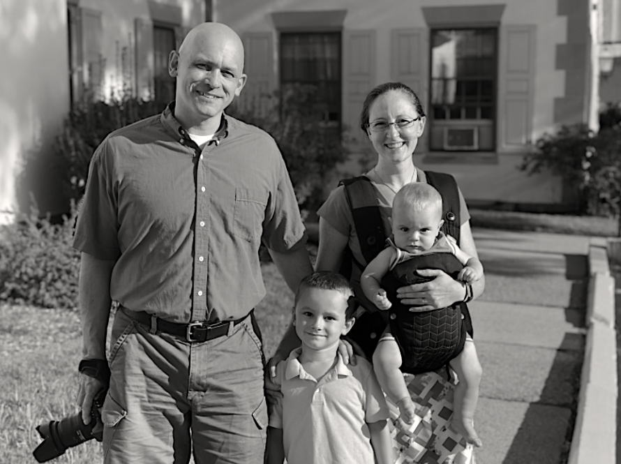 Family of four standing outdoors on a sunny walkway, smiling at the camera.